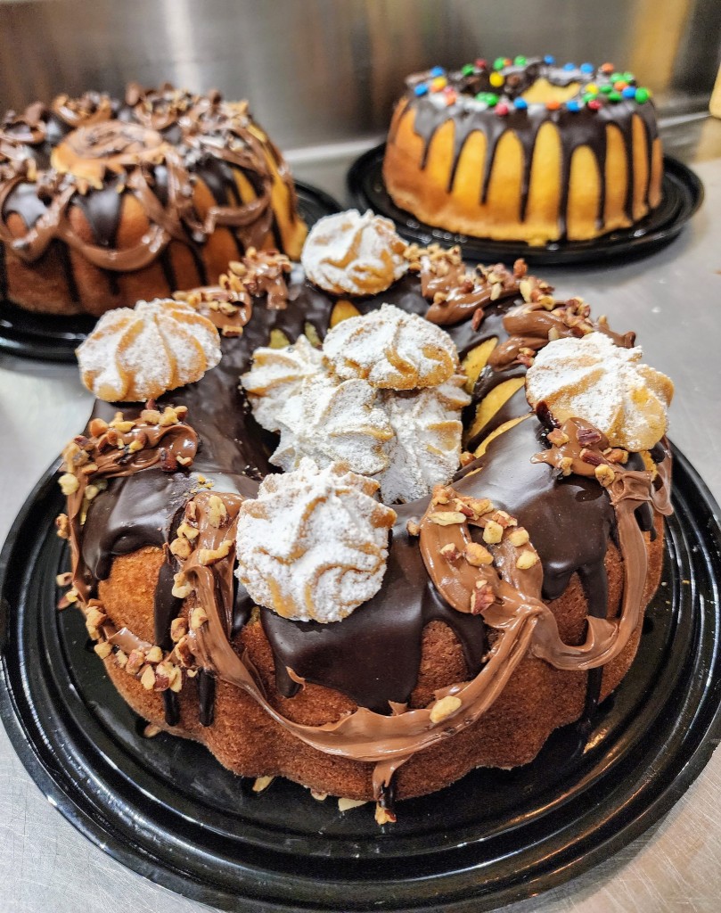 Three decorated bundt cakes with chocolate glaze and toppings