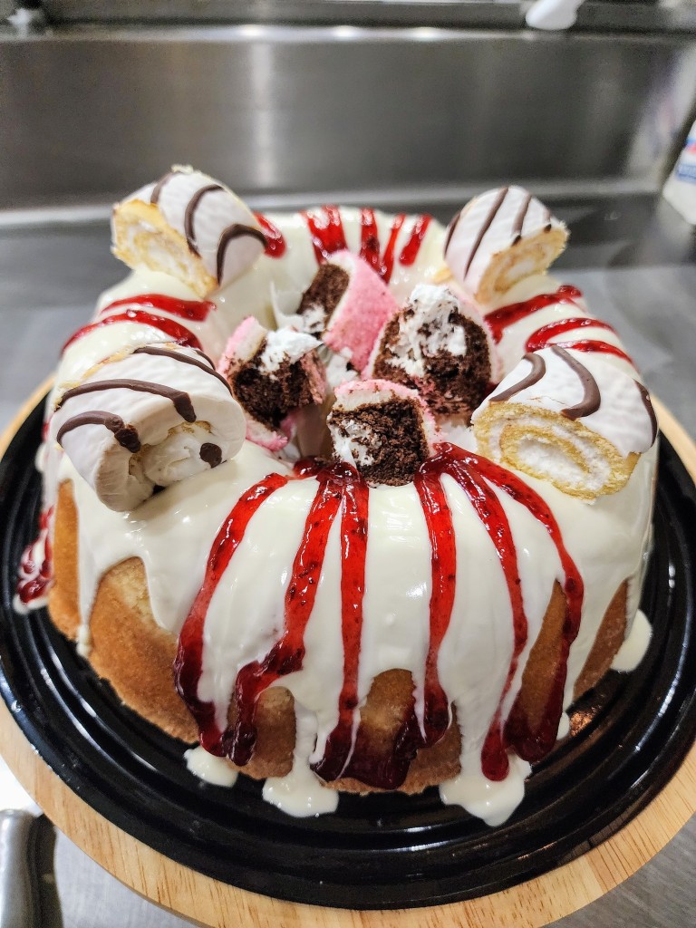 White-glazed bundt cake with berry drizzle and Swiss roll garnish